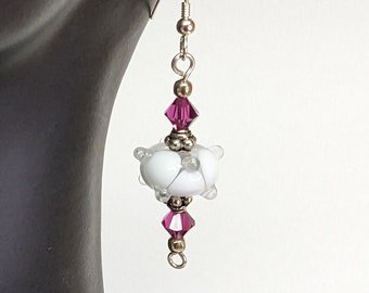 May include: White glass bead earrings with a purple crystal accent. The earrings are silver and have a hook closure.