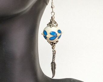 May include: White and blue glass bead earrings with a silver feather charm. The bead has a white background with blue floral designs.