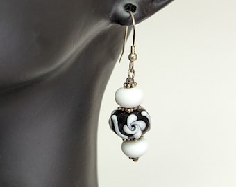 May include: Black and white glass bead earrings with a floral design. The earrings are hanging from silver hooks.