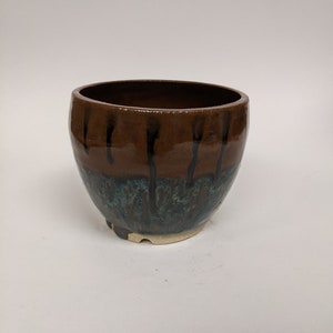 May include: A brown and blue ceramic planter with a drip glaze design. The planter has a rounded shape and a slightly flared rim.