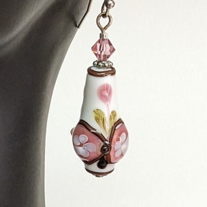 May include: White glass dangle earrings with a pink and brown butterfly design and a pink crystal bead.