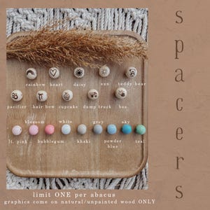 May include: Wooden beads with engraved designs and various colors, including light pink, bubblegum, white, grey, sky, and teal. The beads feature images of a rainbow, heart, daisy, sun, teddy bear, pacifier, hair bow, cupcake, dump truck, and bee.