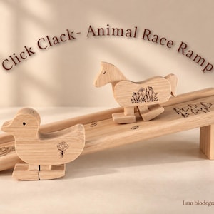 May include: A light-colored wooden animal race ramp with the text Click Clack- Animal Race Ramp. The set includes a wooden horse and a wooden duck, both featuring floral engravings, and the text I am biodegradable with a globe icon.