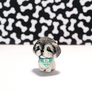 May include: A small, gray and white, hand-painted figurine of a Shih Tzu dog wearing a teal blue bandana with white polka dots and the text "Foster Dogs".
