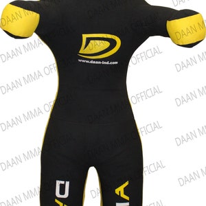 May include: Black and yellow freestanding training dummy with the text "DAAN MMA" on the legs and "www.daan-ind.com" on the chest. The dummy has a target on the chest.