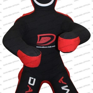 May include: A black and red freestanding punching bag with a white circle target on the chest. The bag has the text "DAAN MMA OFFICIAL" printed on the sides and the text "www.dsan-ind.com" printed on the front.