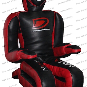 May include: A black and red MMA training dummy. The dummy has a head with a white target circle, a torso, arms, and legs. The text "DAAN MMA OFFICIAL" is printed repeatedly on the sides. The website "www.daan-ind.com" is visible.