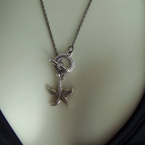 May include: A silver chain necklace with a silver starfish charm and a toggle clasp. The necklace is on a mannequin wearing a black swimsuit.