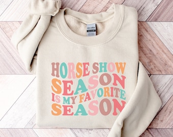 Può includere: Una felpa beige con il testo "Horse Show Season is my Favorite Season" in lettere retrò colorate.