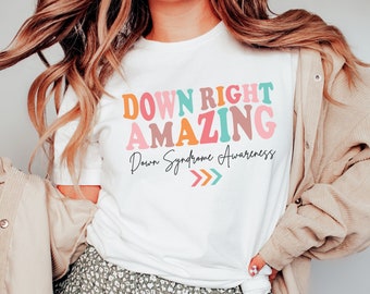 May include: White t-shirt with the text "Down Right Amazing" in colorful letters. The text "Down Syndrome Awareness" is written in black below the main text. Three arrows point to the right.