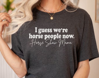 Può includere: Una maglietta grigio scuro con il testo "I guess we're horse people now. Horse Show Mama" in bianco.