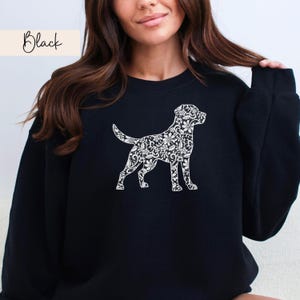 May include: Black sweatshirt featuring a white floral dog silhouette. The word "Black" is written in cursive in the upper left corner. The sweatshirt is a solid black color and has a crew neck.