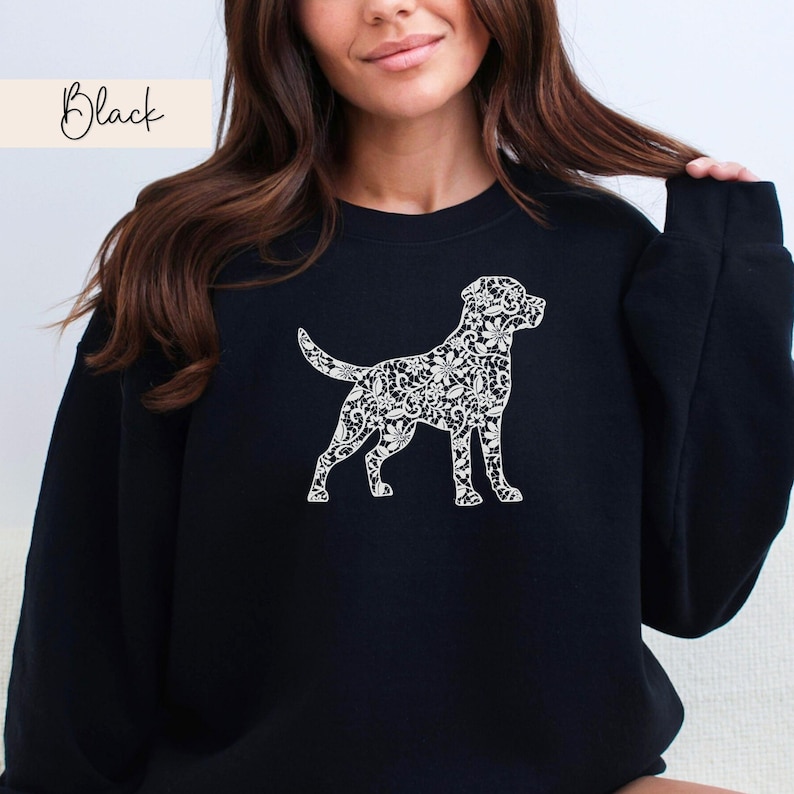May include: Black sweatshirt featuring a white floral dog silhouette. The word "Black" is written in cursive in the upper left corner. The sweatshirt is a solid black color and has a crew neck.