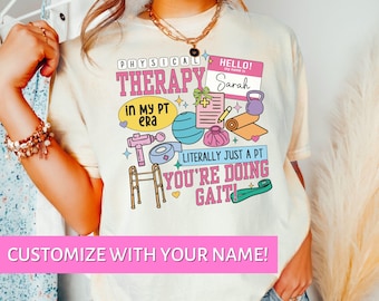 May include: Cream-colored t-shirt with a colorful graphic design related to physical therapy. The design includes the text "PHYSICAL THERAPY" and "LITERALLY JUST A PT YOU'RE DOING GAIT". The shirt also has the text "CUSTOMIZE WITH YOUR NAME!"
