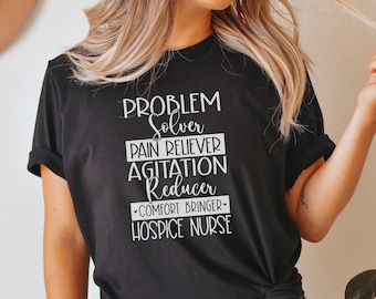 May include: Black t-shirt with white text that reads "Problem Solver, Pain Reliever, Agitation Reducer, Comfort Bringer, Hospice Nurse".