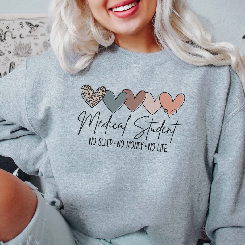 May include: A light gray sweatshirt with the words "Medical Student" in black script, accompanied by four heart designs in various colors and patterns. Below the text are the words "NO SLEEP &bull; NO MONEY &bull; NO LIFE."