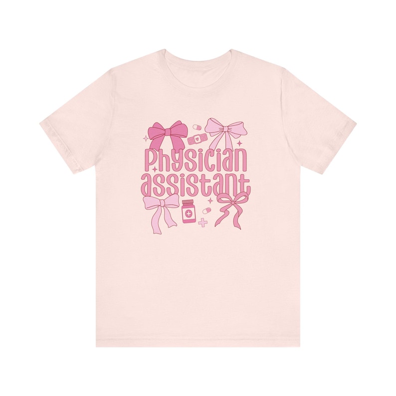 May include: Pink t-shirt with the text "Physician Assistant" in pink lettering. The text is surrounded by pink bows, pills, and a bandage.