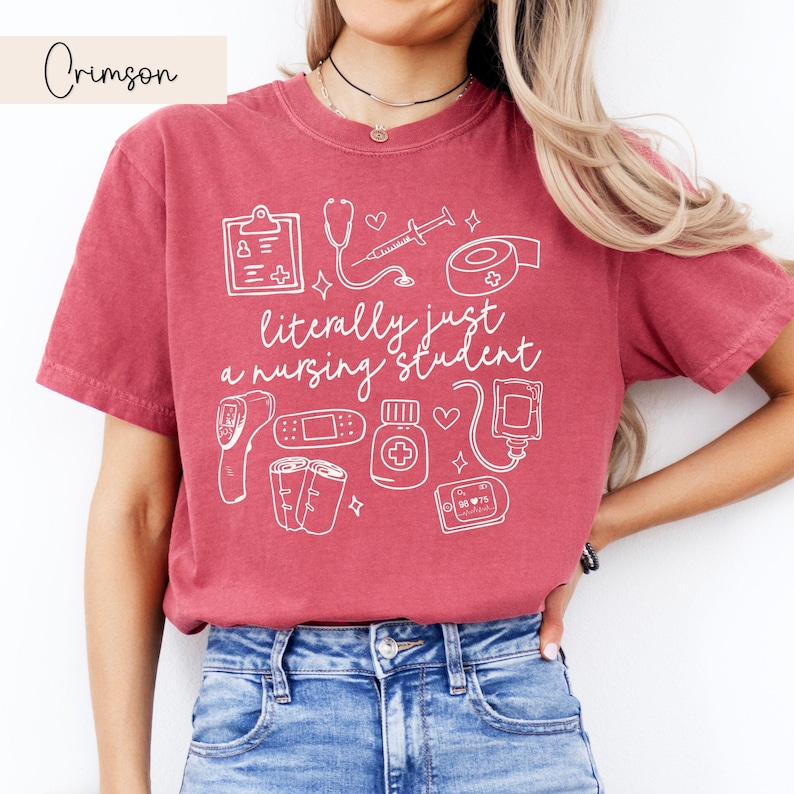 K&ouml;nnte beinhalten: Ein T-Shirt in Rotbraun mit einem wei&szlig;en Grafikdesign von medizinischen Utensilien und dem Text "literally just a nursing student".