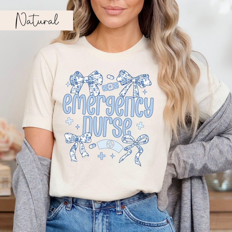 May include: A white t-shirt with the text "emergency nurse" in blue lettering. The shirt is decorated with blue bows and medical symbols.