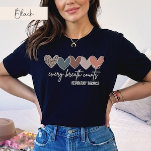 以下が含まれることがあります： 5つのカラフルなハートと「every breath counts」と「RESPIRATORY THERAPIST」のテキストが描かれた黒いTシャツ。
