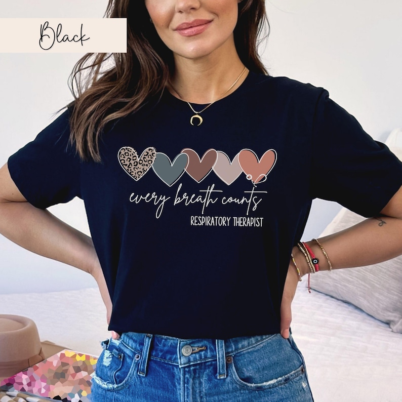 以下が含まれることがあります： 5つのカラフルなハートと「every breath counts」と「RESPIRATORY THERAPIST」のテキストが描かれた黒いTシャツ。