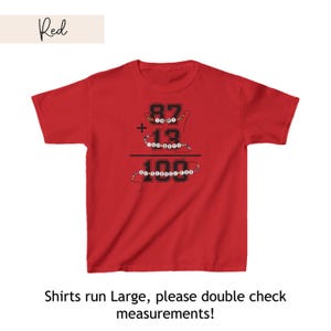 May include: Red t-shirt with a graphic of a math equation: 87 + 13 = 100. The numbers are surrounded by colorful beads. The text "Shirts run Large, please double check measurements!" is below the graphic.