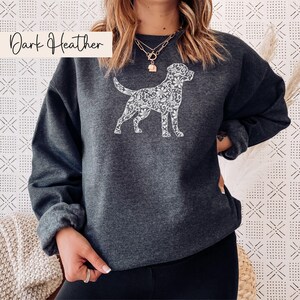May include: Dark heather gray sweatshirt featuring a white floral dog silhouette. The text "Dark Heather" is in the upper left corner. The sweatshirt has long sleeves and a crew neck.