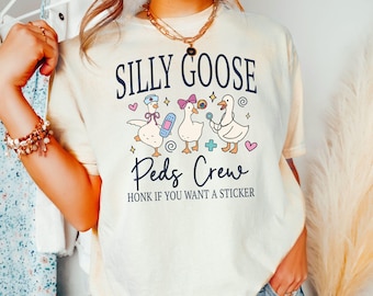 May include: Cream-colored t-shirt with the text "SILLY GOOSE Peds Crew" and an illustration of three cartoon geese. The geese are wearing a nurse's hat, a bow, and holding medical items. The text "HONK IF YOU WANT A STICKER" is below.
