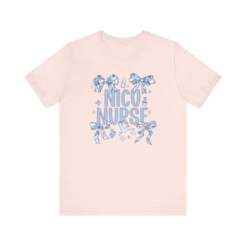 May include: Pink t-shirt with a blue design that says "NICU Nurse" surrounded by bows, baby bottles, and other baby-related imagery.