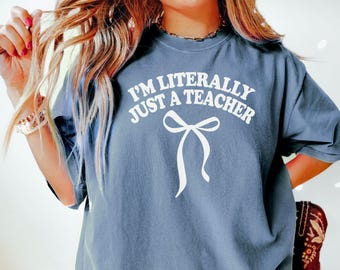 May include: A blue t-shirt with the text "I'm literally just a teacher" in white with a white bow underneath.