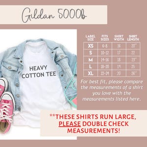 May include: White Gildan 5000b t-shirt with the text "Heavy Cotton Tee" printed on the front. The shirt is laid flat on a surface with a denim jacket and pink sneakers. A size chart is shown with the label size, fits sizes, shirt width in inches, and shirt length in inches.