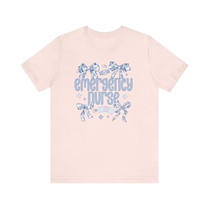May include: Pink t-shirt with a blue and white floral design and the text "emergency nurse".