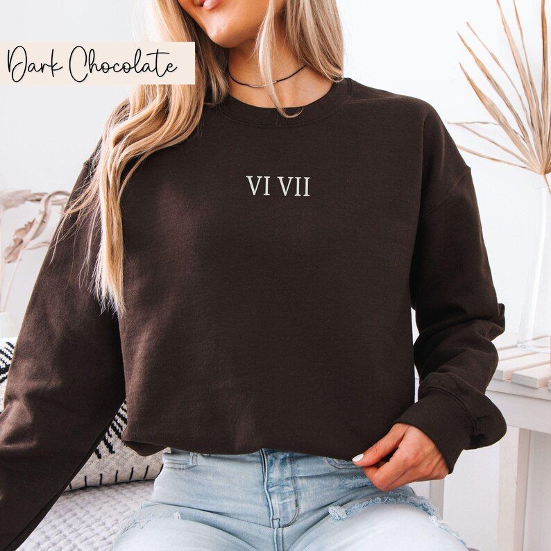 May include: Dark chocolate-colored sweatshirt with the Roman numerals VI VII printed in white. The sweatshirt has a crew neck and long sleeves. The words "Dark Chocolate" are in a cursive font in the upper left corner.