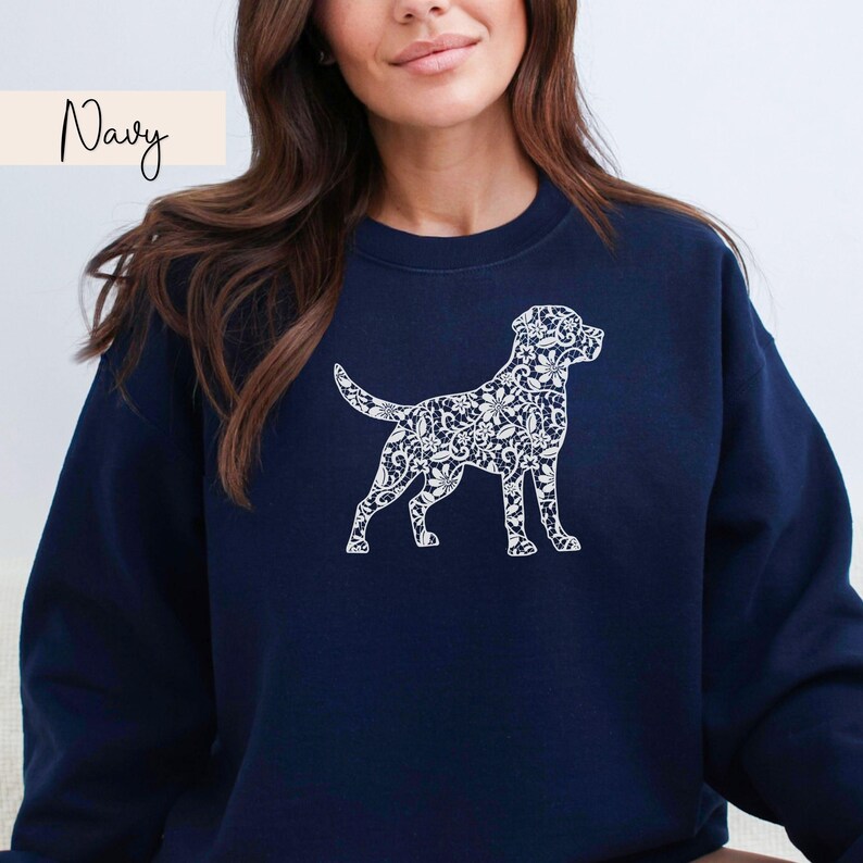 May include: Navy blue sweatshirt featuring a white floral patterned dog silhouette. The word "Navy" is written in cursive in the upper left corner. The sweatshirt is a solid navy color.