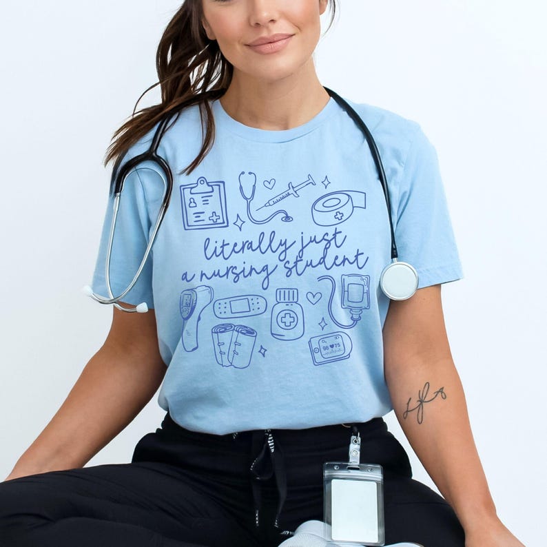 May include: A light blue t-shirt with a graphic of medical supplies and the text "literally just a nursing student".