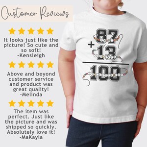 May include: White t-shirt with a black and white graphic of a math equation. The equation reads "87 + 13 = 100". The numbers are surrounded by colorful beads. The text "100 Days of School" is written below the equation.