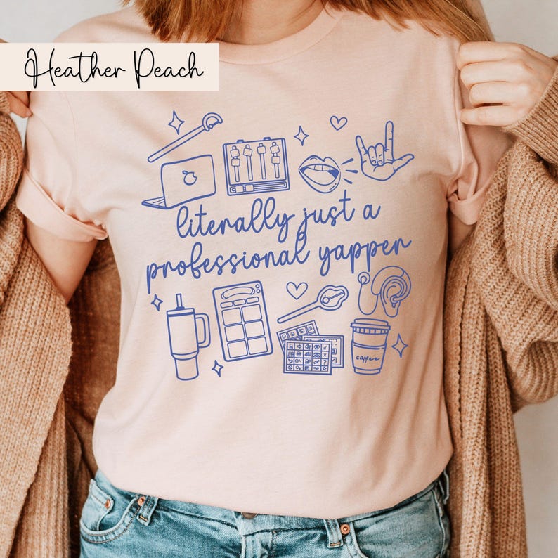 以下が含まれることがあります： ピンクのTシャツに、青いグラフィックデザインが施されています。デザインには、「ただのプロのしゃべり屋」という文字が書かれています。グラフィックには、マイク、ラップトップ、コーヒーカップ、ミキシングボード、ハート、愛してるのサインをする手、ヘッドホン、サイコロが描かれています。