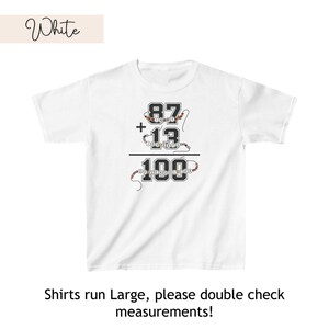 May include: White t-shirt with a black and white graphic of a math equation: 87 + 13 = 100. The numbers are made of colorful beads. The text "Shirts run Large, please double check measurements!" is printed below the graphic.