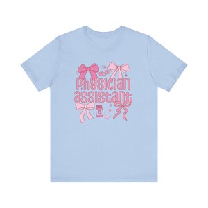 May include: Light blue t-shirt with a pink graphic design featuring the text "Physician assistant" with bows, pills, and bandages.