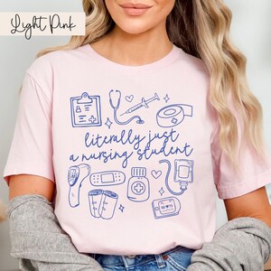May include: Light pink t-shirt with a blue graphic of medical supplies and the text "literally just a nursing student".