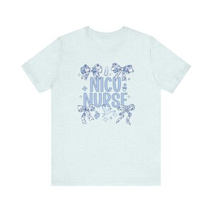 May include: Light blue t-shirt with a blue and white floral design. The shirt has the text "NICU NURSE" with a variety of small blue and white icons.