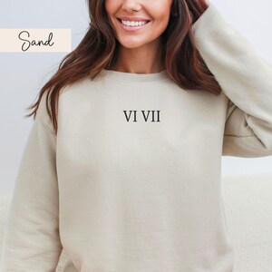 May include: A sand-colored sweatshirt with the Roman numerals VI VII printed in black. The sweatshirt has a crew neck and long sleeves. The word "Sand" is written in cursive in the upper left corner.