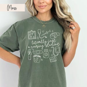K&ouml;nnte beinhalten: Ein gr&uuml;nes T-Shirt mit einem wei&szlig;en Grafikdesign von medizinischen Ger&auml;ten und dem Text "im Grunde nur ein Krankenpflegesch&uuml;ler".