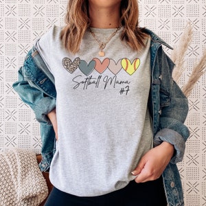 May include: Gray t-shirt with a graphic of five hearts, each with a different pattern. The hearts are arranged horizontally. The text "Softball Mama #7" is printed below the hearts.