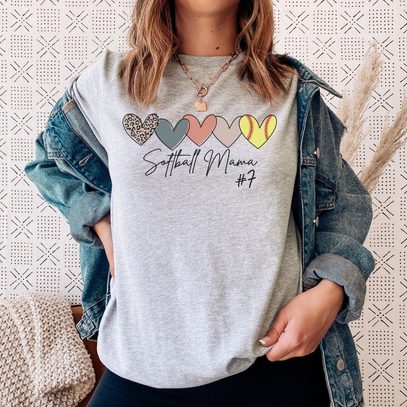May include: Gray t-shirt with a graphic of five hearts, each with a different pattern. The hearts are arranged horizontally. The text "Softball Mama #7" is printed below the hearts.