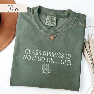 May include: A green t-shirt with the text "CLASS DISMISSED NOW GO ON... GIT!" in white. The shirt features a small outline of two cowboy boots.