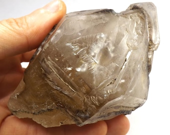 May include: A large, clear quartz crystal with a smoky brown hue. The crystal has multiple facets and a rough, natural texture.