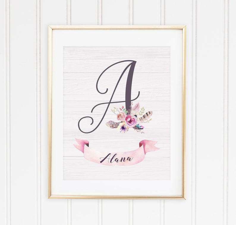 May include: A framed print with a white woodgrain background featuring a large cursive letter A with pink and purple flowers and feathers. A pink ribbon banner with the name "Alana" is below the letter.