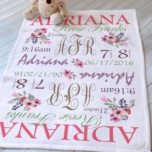May include: A white personalised baby blanket featuring the name Adriana Reese Franks, birth date 06/17/2016, time 9:16am, length 21 inches, and weight 7 pounds 8 ounces. The design includes floral accents, the monogram AFR, and a plush bear.