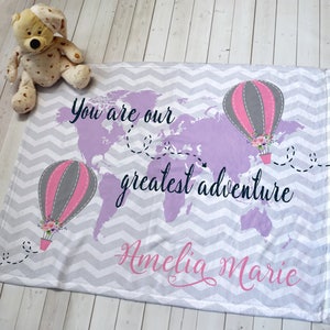 May include: A soft, gray and white chevron patterned baby blanket with a purple world map and hot air balloons. The text "You are our greatest adventure Amelia Marie" is printed on the blanket.
